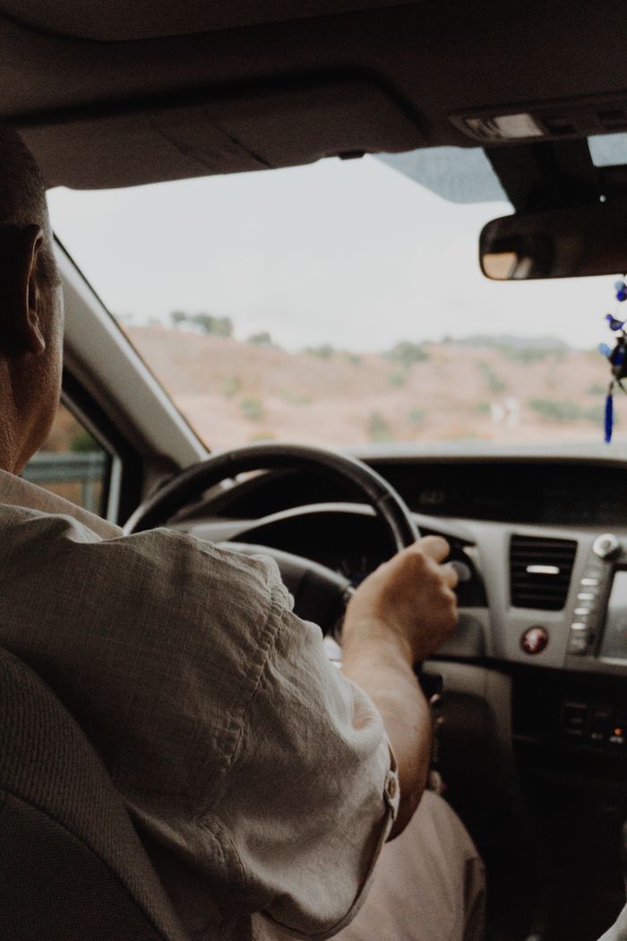 Rear view of a person driving a car on a road trip through hilly landscape.