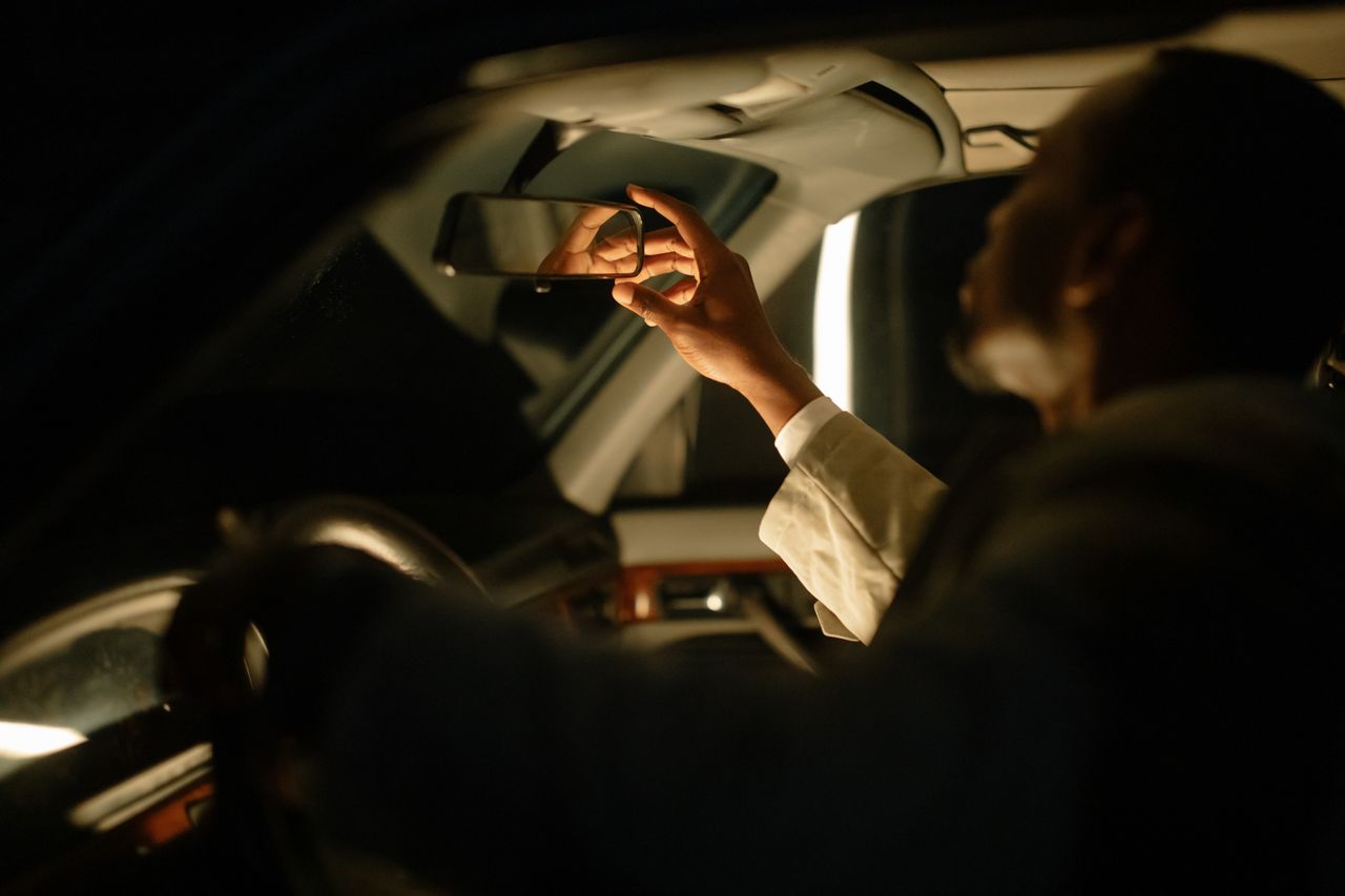 services-02 A man adjusting the rear view mirror inside a car, captured during nighttime with soft lighting.