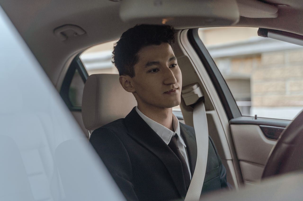 hero-img-01 Young professional driver in formalwear inside a modern car, looking focused and attentive.