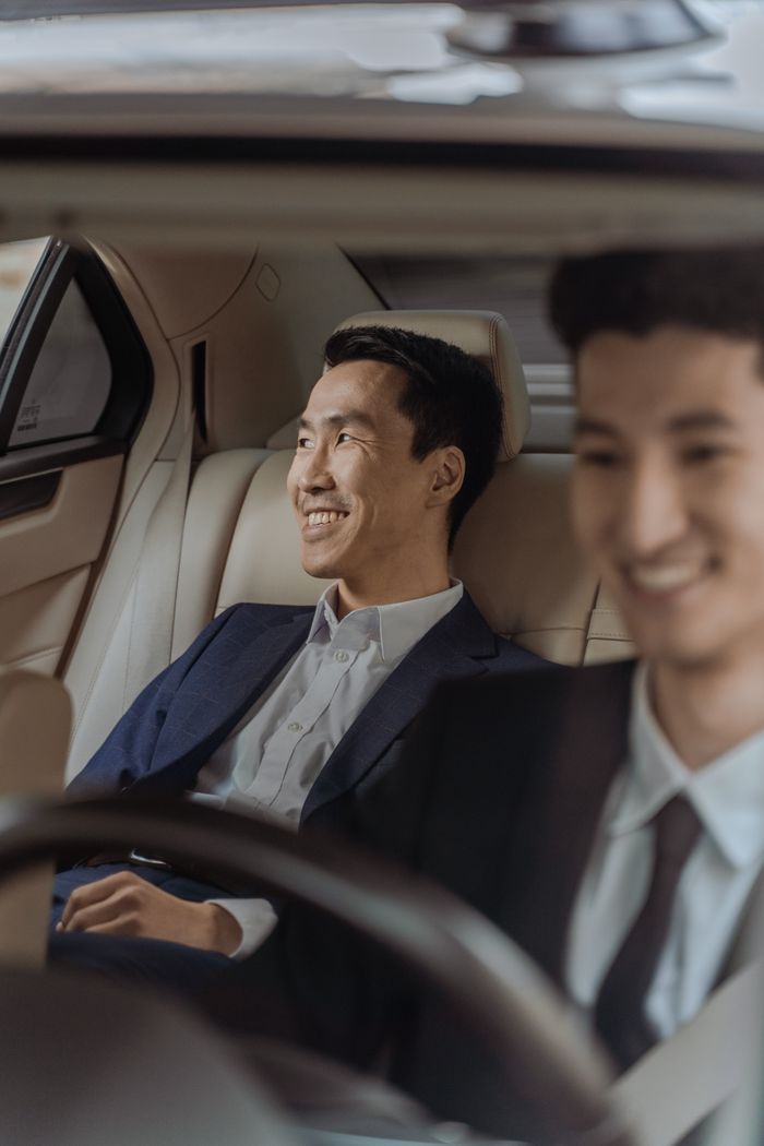 gallery-3 Two men in formalwear enjoying a comfortable ride in a luxury car, smiling.
