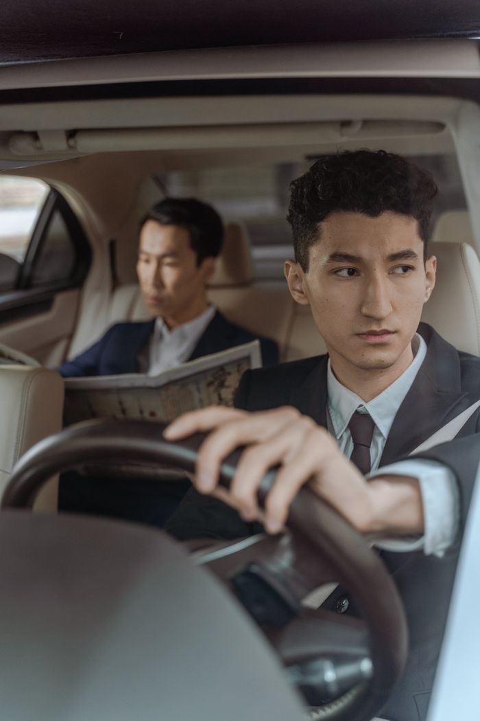 gallery-4 Professional chauffeur driving with attentive passenger reading in a luxury car interior.